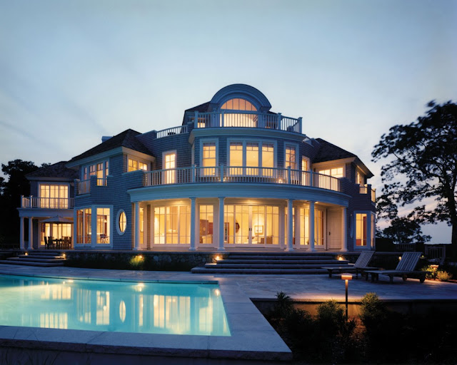Elegant mansion lit up at dusk with a swimming pool and lounge chairs in front, blue and warm amber tones, calm evening mood
