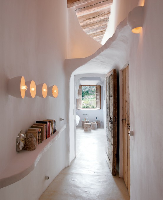 A curved white plaster hallway with warm wooden beams, soft wall sconce light and rustic doors, warm and inviting